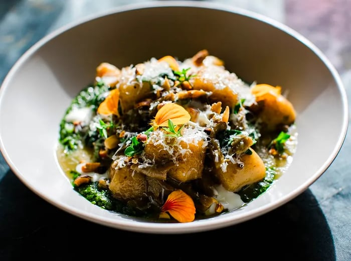 A plate of roasted vegetables adorned with grated cheese and edible blooms.