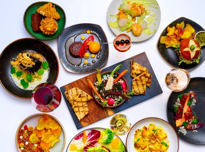 An assortment of various vegetable and meat dishes displayed on an array of mismatched stoneware against a white backdrop.