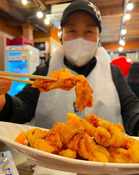 A woman in a mask holds up chopsticks with food in them.