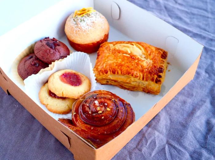 An open paper box displaying an assortment of baked goods and cookies