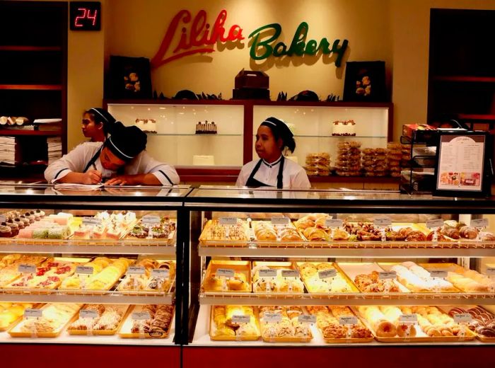 A well-lit pastry display filled with delectable treats, with staff working behind the counter and the name Liliha Bakery prominently displayed in large block letters on the back wall