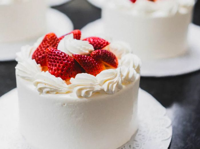 Delicate small cakes displayed on individual plates, adorned with white frosting and topped with vibrant strawberry slices