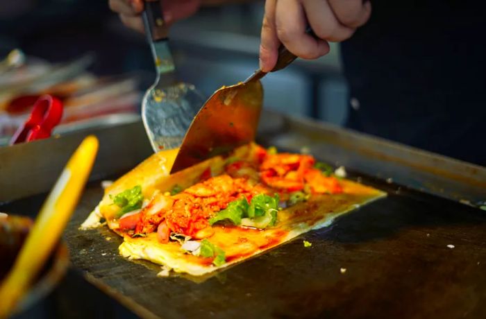 A spatula deftly folds a stuffed jianbing pancake.