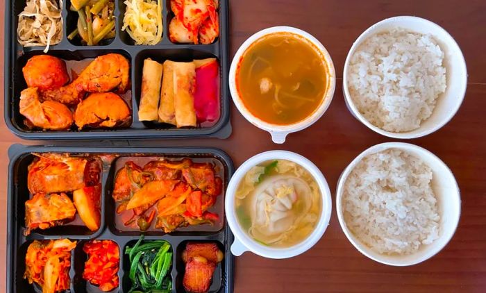 Two food containers accompanied by bowls of rice and soup.