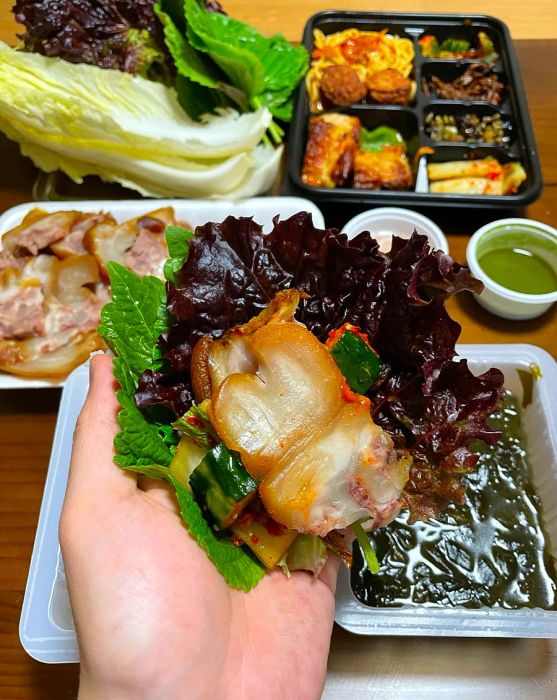 A hand holds leafy greens filled with pieces of pork inside.