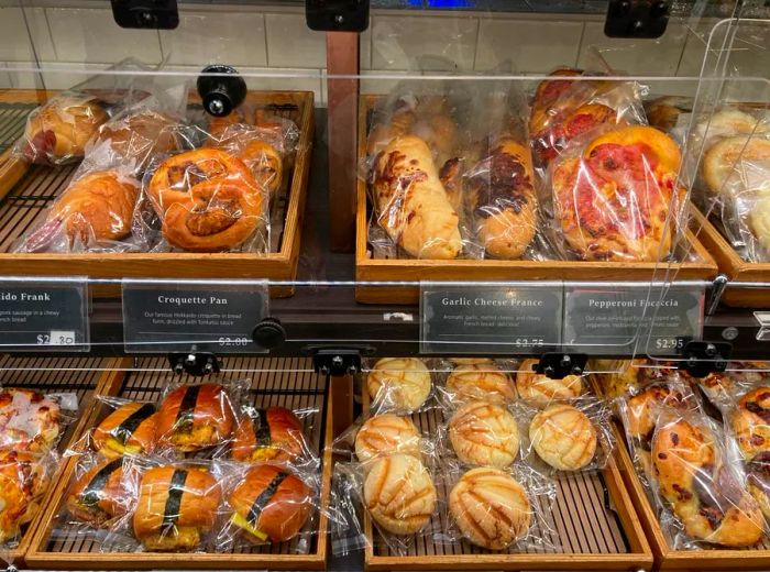 A pastry display filled with wooden boxes showcasing a variety of muffins, cookies, and individually wrapped sweets in cellophane