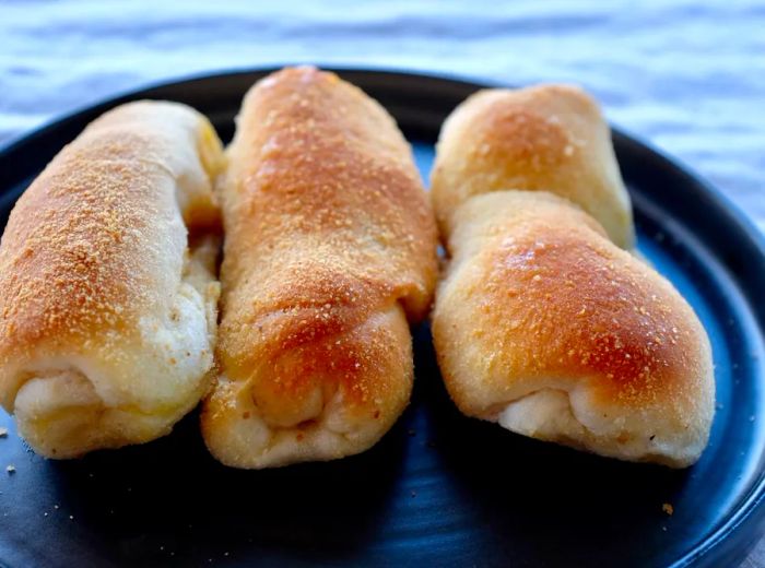 Three elongated twisted pastries arranged on a dark plate