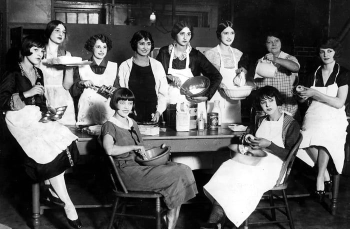 A historic photograph of women seated in chairs, learning to cook.