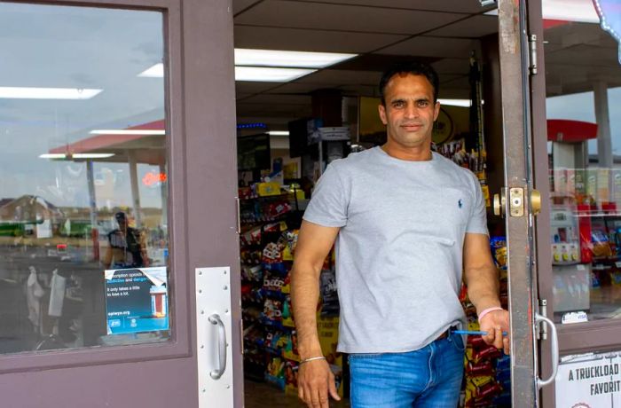 A man in a t-shirt opens the door to a store, facing the viewer.