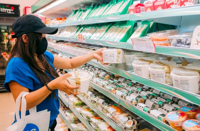 A woman selects a bowl of ramen from a shopping aisle.