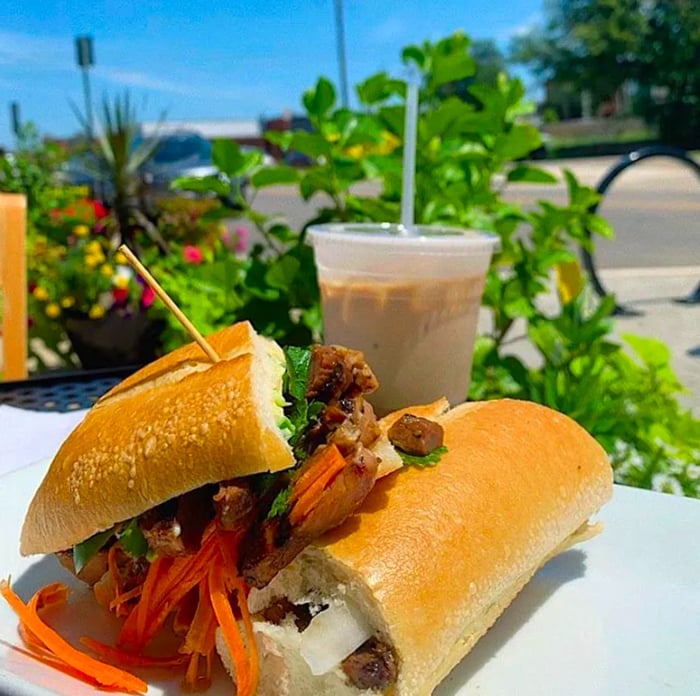 A banh mi sandwich placed on an outdoor table alongside a takeout drink