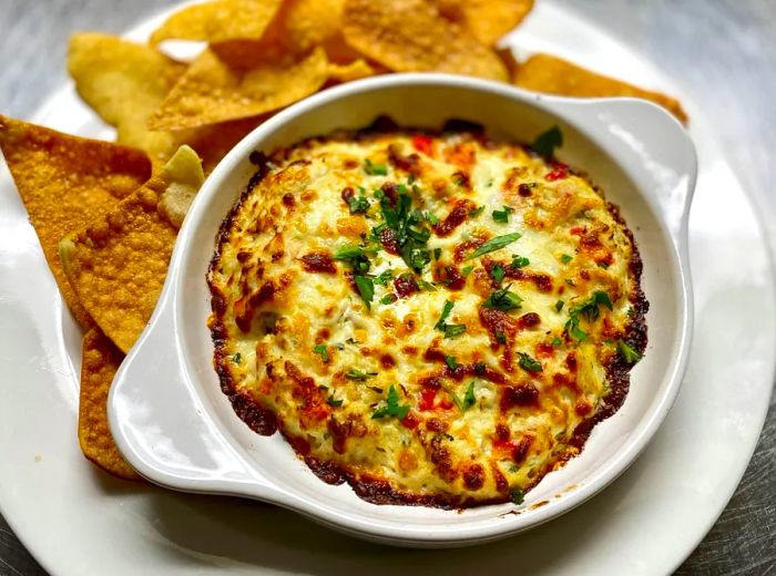 A bowl filled with crab dip surrounded by crispy chips