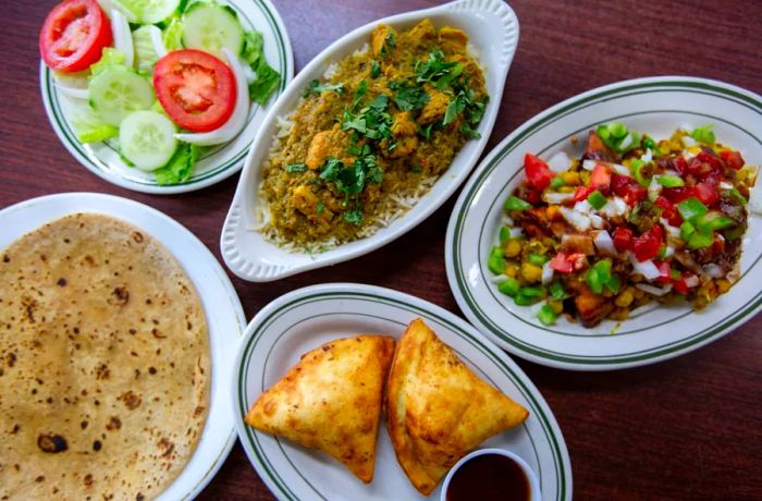 Aerial view of dishes arranged on a table, displaying plates of chicken curry, roti, samosas, and a green salad.