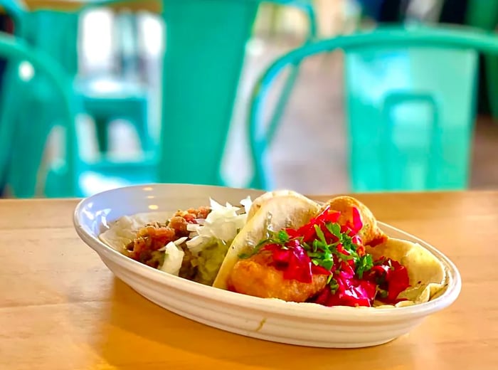 A platter of tacos resting on a table next to vibrant metal chairs