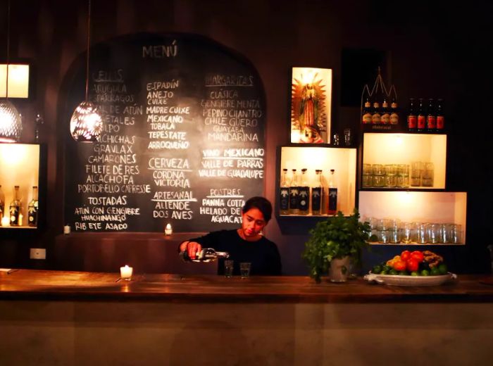 A woman serves a drink at the bar, with a chalkboard menu displayed behind her.