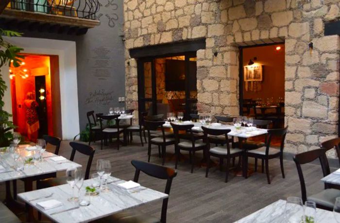 Wooden tables paired with wooden chairs set against a stone wall.