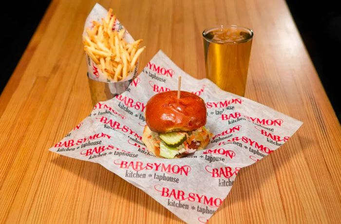 A sandwich plated on branded butcher paper, accompanied by fries and a beer.