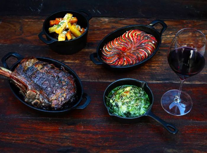 A steak accompanied by side dishes served in cast iron cookware on a wooden table.