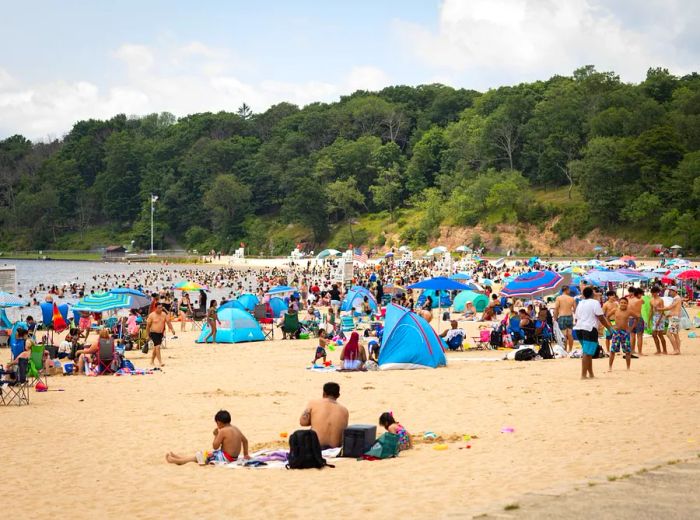 numerous people gathered along the shores of a lakeside beach.