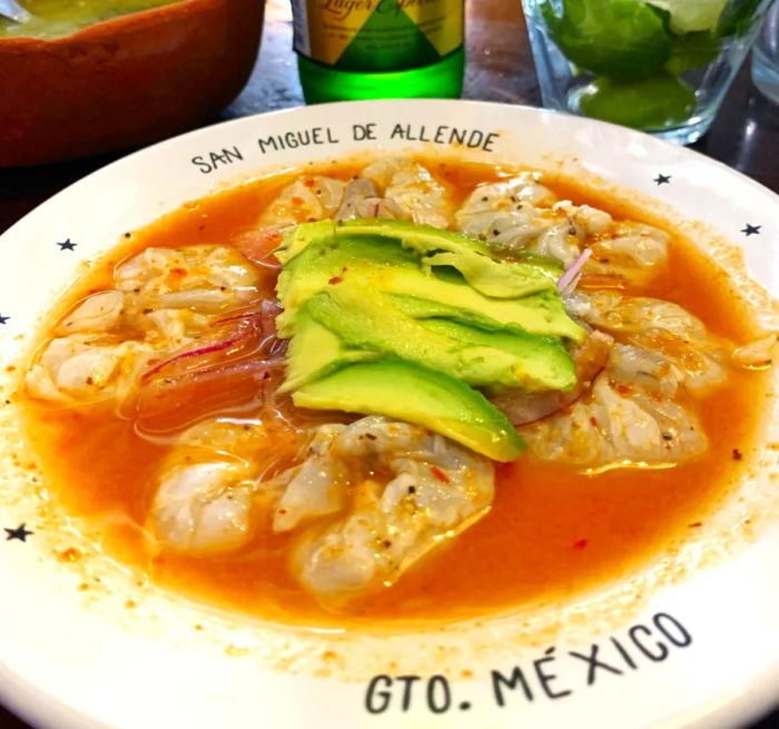 Shrimp served in a bowl, garnished with avocado, with a beer in the background.