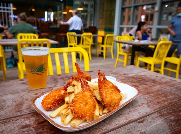 Coconut shrimp served atop a bed of fries on a wooden table, with yellow chairs in the background.