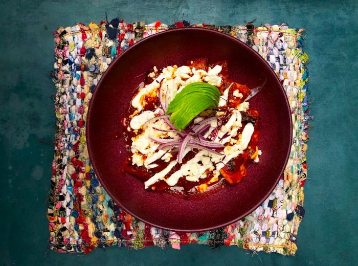 A round bowl filled with dark food accompanied by a white sauce and a lime, placed on a placemat.