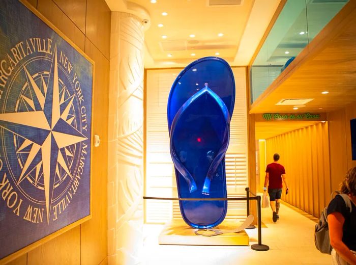 A massive blue flip-flop sits behind glass in a corridor as a man strolls by.