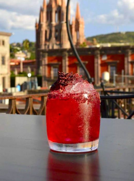 A vibrant red drink in a glass on a table, with a cathedral view in the background.