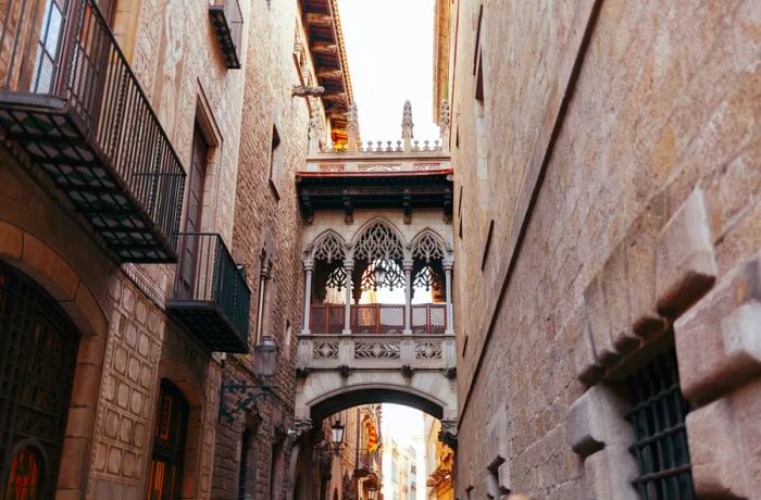 An elaborate footbridge spans a walkway in historic Barcelona.