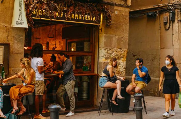 Men and women relax on stools outside a vermouth bar.