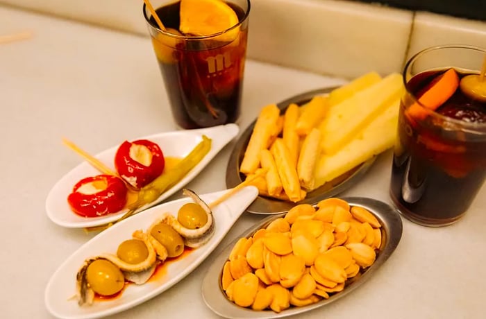 Two glasses of vermouth accompany various plates of snacks, including almonds and olives.