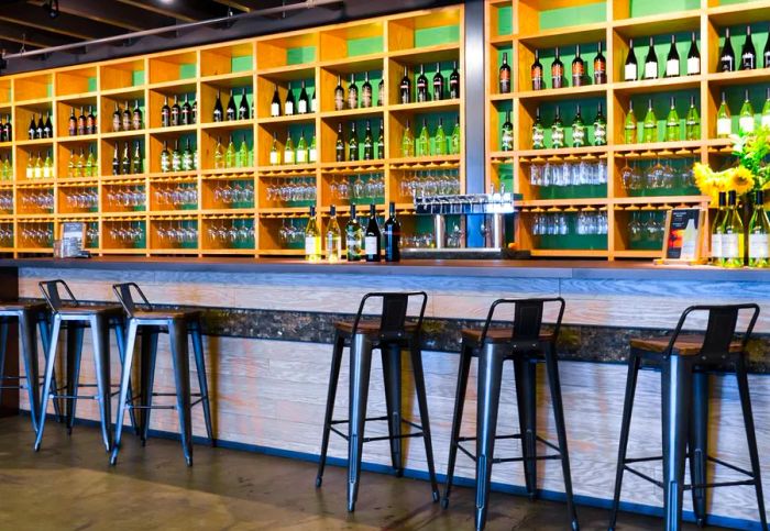 A bar featuring an array of wine bottles lining the back and metal stools for seating.