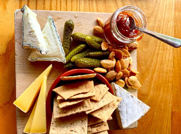 A wooden table featuring a selection of cheese varieties, accompanied by a stack of crackers and a jar of jam.