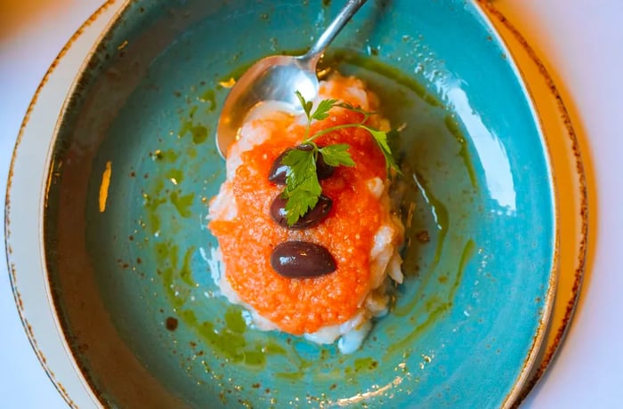 A blue-green plate piled high with shredded fish, garnished with tomato sauce and olives.