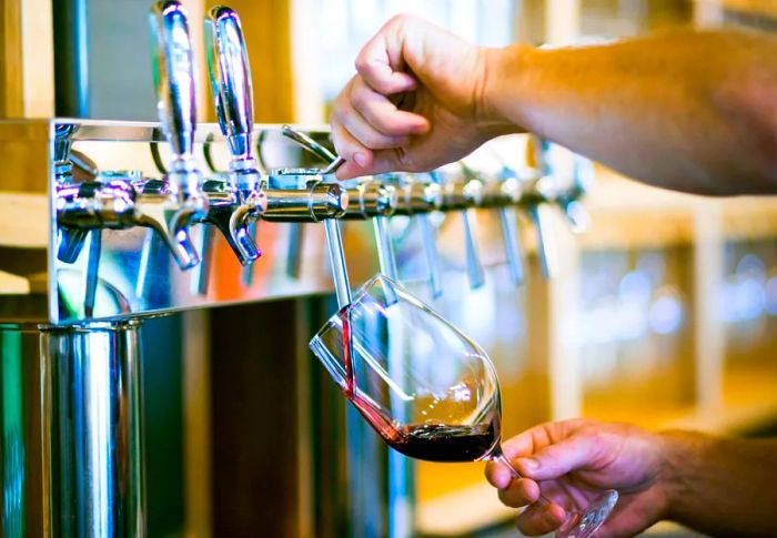 A person pours red wine from a tap into a glass.