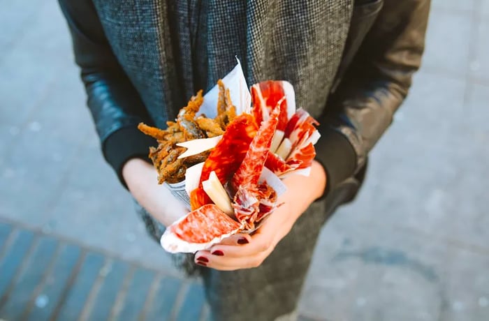 Two hands cradling paper cones filled with an assortment of meats and fish, resembling a bouquet, in front of a torso.