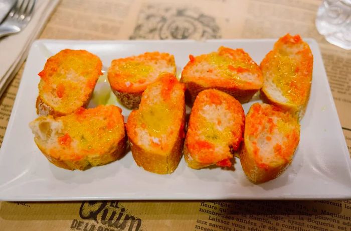 A plate featuring several slices of bread, generously drizzled with olive oil and rubbed with ripe tomato.