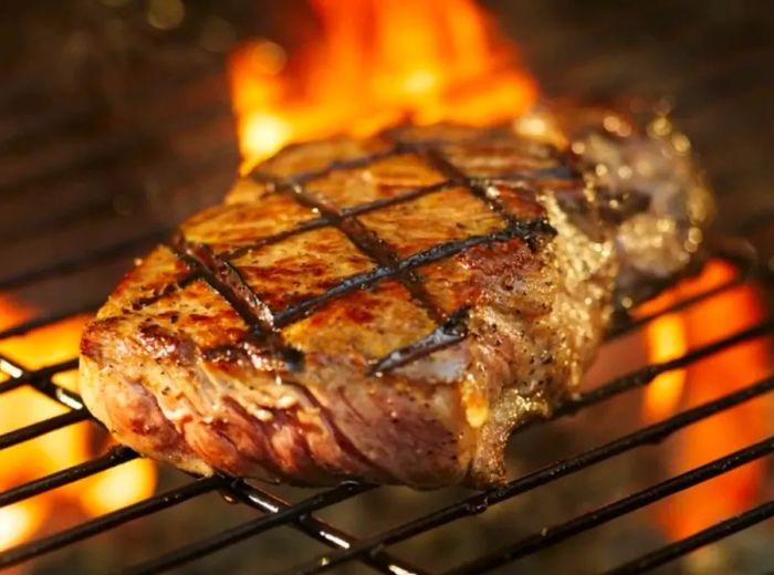 A juicy steak sizzling on the grill, flames dancing in the background.