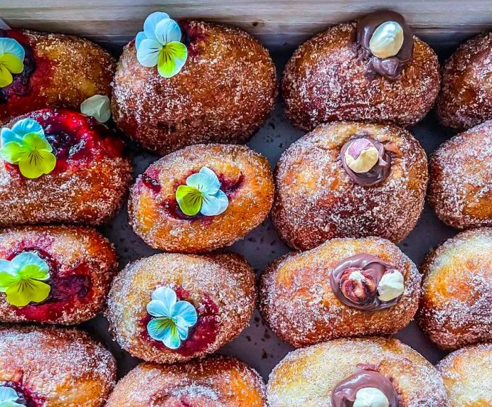 A variety of cream-filled donuts adorned with flowers and other decorations, neatly arranged in a box.