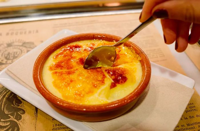 A dish featuring caramelized crema catalana, with a spoon sinking into its center.