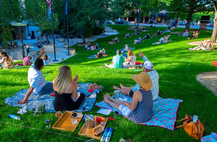 Groups of people enjoy a picnic on a grassy hill.