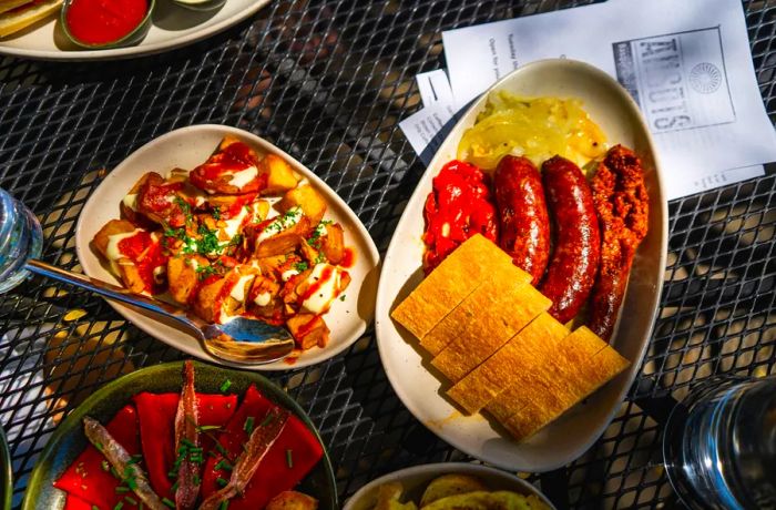 A spread of dishes on a metal outdoor table, featuring chorizo and potatoes.