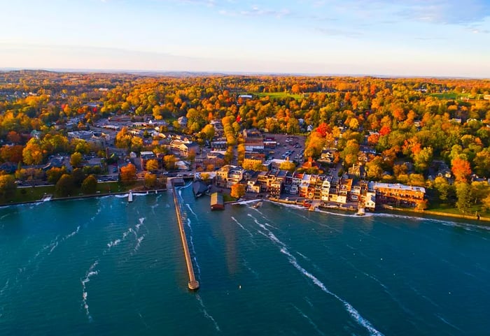 A quaint town overlooks a lake, framed by vibrant fall foliage in the background.