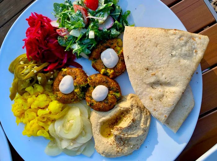 An overhead shot of a platter filled with falafel balls, surrounded by a fresh salad, vibrant pickled vegetables, a generous scoop of hummus, and wedges of flatbread.