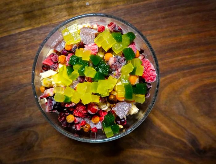 An overhead view of a bowl of bingsoo filled with colorful bits of fruit, jelly, and shaved ice arranged in bright shapes.