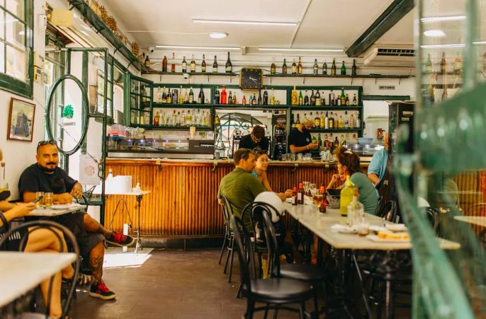 Groups of patrons gathered around a rustic wooden bar adorned with bottles on display.