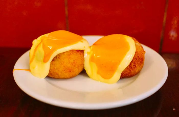 Two croquettes drizzled with yellow and orange sauces on a plate.