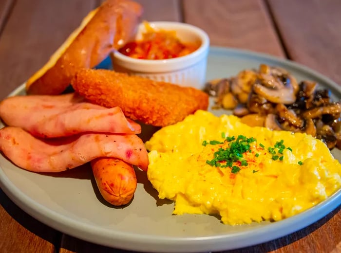 A plate filled with eggs alongside breakfast meats, mushrooms, and various fried items.