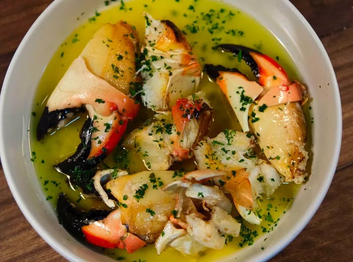 A dish featuring crab claws swimming in a buttery herb sauce.