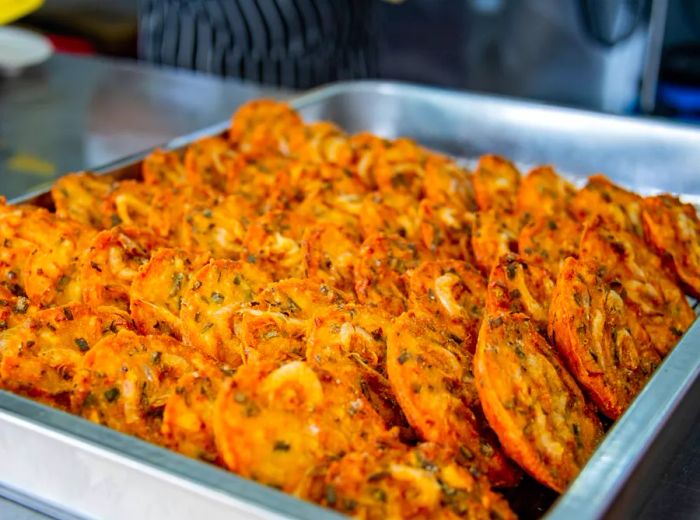 A metal tray filled with rows of cucur udang (prawn fritters) stacked neatly.